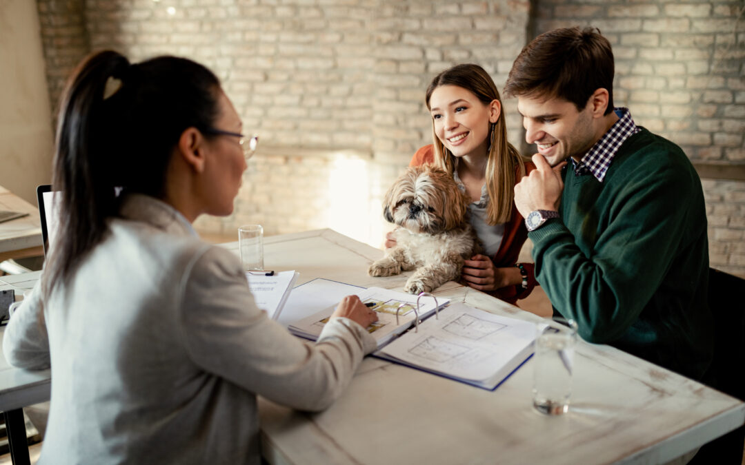 “Pareja joven reunida con su agente inmobiliario para revisar el contrato de compraventa de una vivienda.”